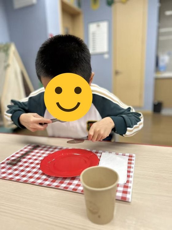 A student practising holding a knife and fork at his place setting